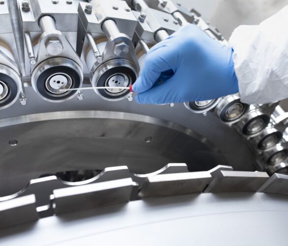 Close-up of a hand in a blue glove cleaning a technical component of a large industrial machine with a swab.